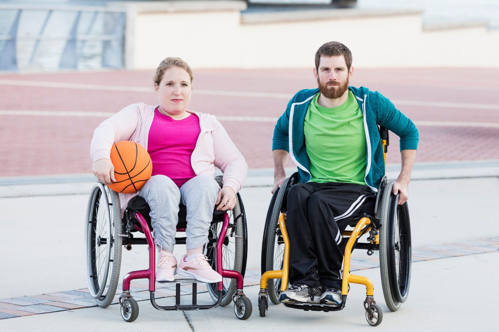 A woman and a man in wheelchairs pose outdoors as she holds a basketball.