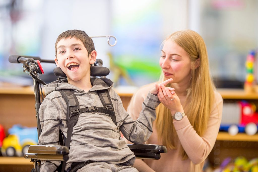 Disabled child on a wheelchair with their guardian sitting beside them.