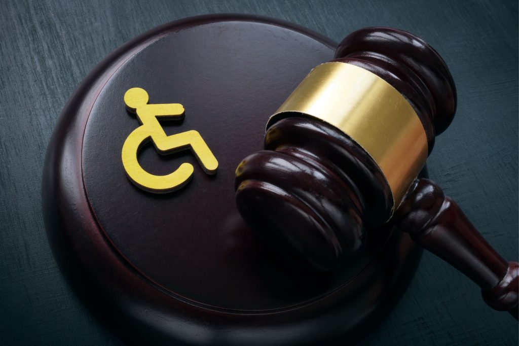 A judge's gavel on a dark table beside a yellow wheelchair symbol, representing legal issues and rights for people with disabilities.