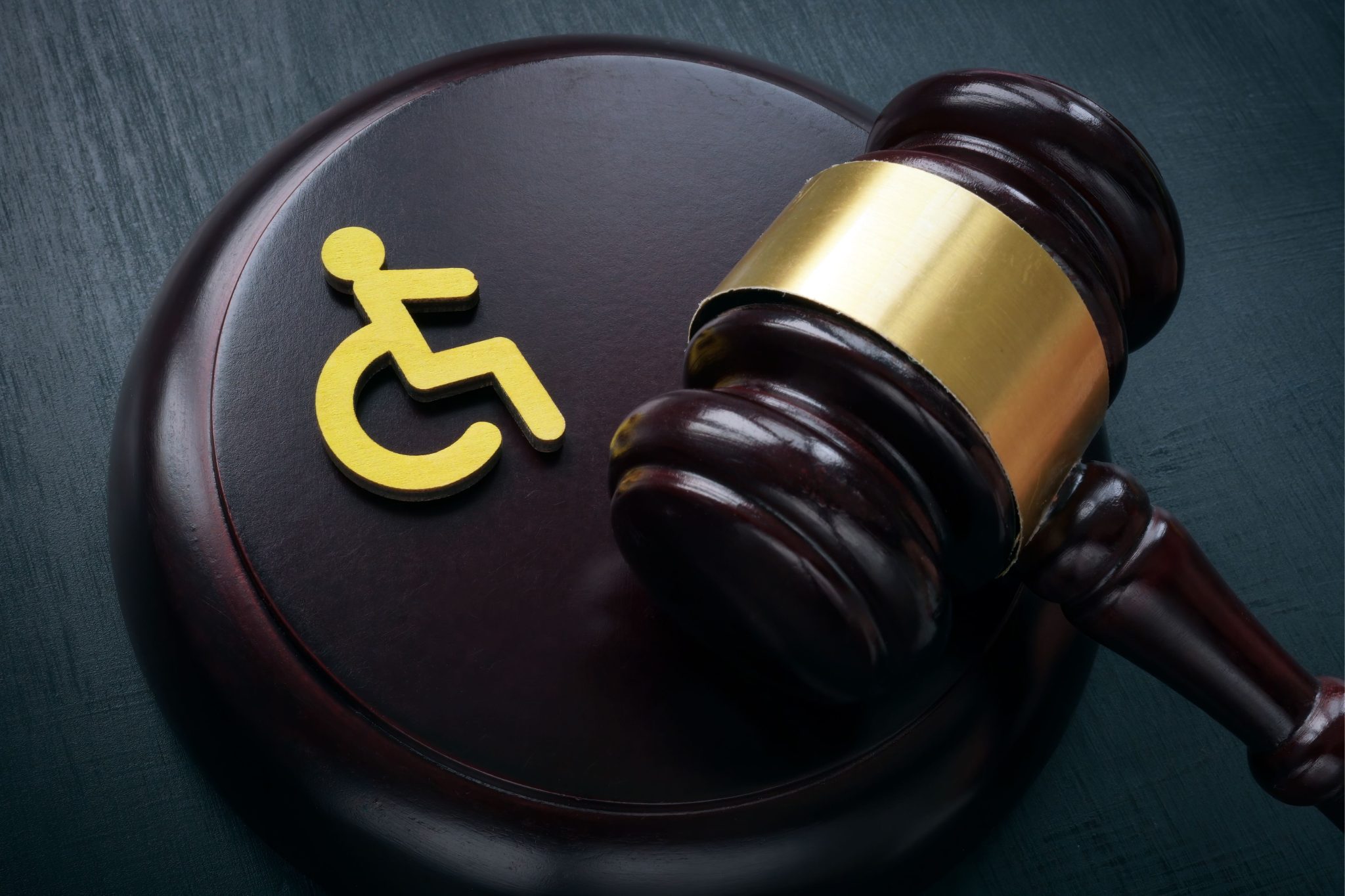 A judge's gavel on a dark table beside a yellow wheelchair symbol, representing legal issues and rights for people with disabilities.