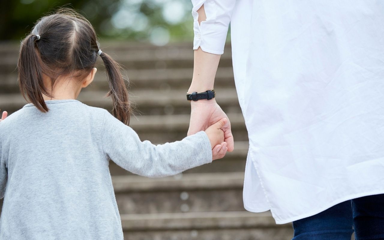 A woman holds the hands of a child with pigtails while ascending outdoor steps.