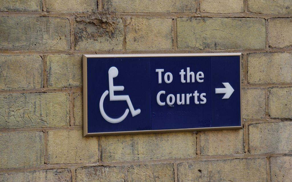 A direction sign for persons with disability on a stone wall. Text says to the courts with an arrow pointing to the right.