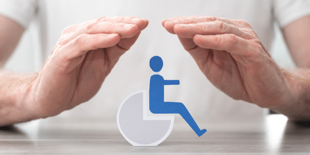 A man holds out his palms in a protective covering over a cut out of a person on a wheelchair sitting on a table.