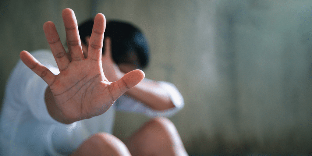 A person seated on the floor with their head down and palm of their right hand stretched out before them.